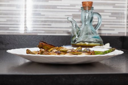 Artichokes and asparagus cooked on the grill in a pan and served on a round white plate and olive oilの写真素材