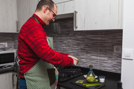 A man in a red fleece and a green apron cooking grilled artichokes and asparagus in a kitchen. He is cutting artichokes.の写真素材