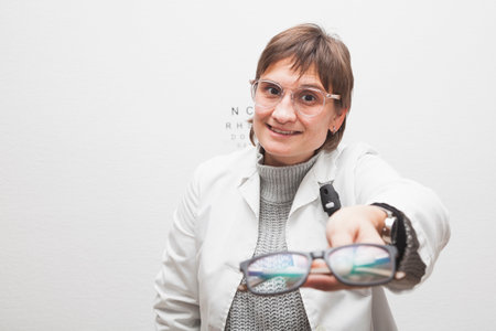 An optician's employee hands a customer new glasses, seen in the first person. The glasses are out of focus and the optometrist's face is in focus.の写真素材