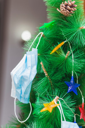 Detail shot of a Christmas tree with star-shaped lights, decorated with blue surgical masks. The...