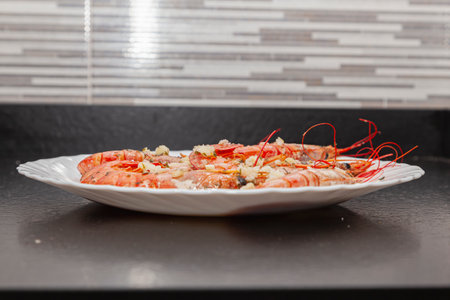 Grilled shrimp served on a round white plate on a black granite kitchen bench. The prawns are seasoned with mince made with oil, garlic and parsley.の写真素材