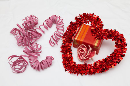A decorative red heart, a gift, a pink flower and pink streamer ribbons on a white fabric as a background.の写真素材