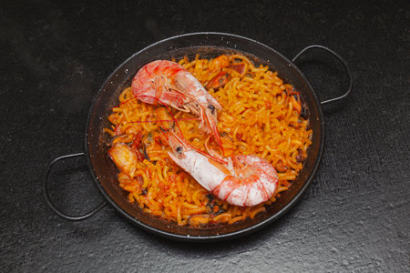 Presentation in a paella of a finished recipe of fideua on a kitchen bench. The recipe calls for broth, thick noodles, fish, squid, shellfish, prawns, mussels, onion, garlic, oil and salt; all ready to eat.の写真素材