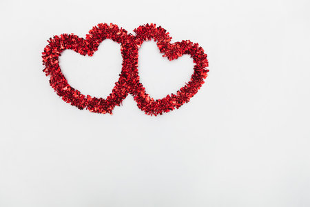 Two red decorative hearts located near the upper right corner of the image placed on a white fabric.の写真素材