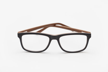 A pair of dark-rimmed glasses viewed from the front, with the temples crossed and placed on a white surface. The background is white.の写真素材