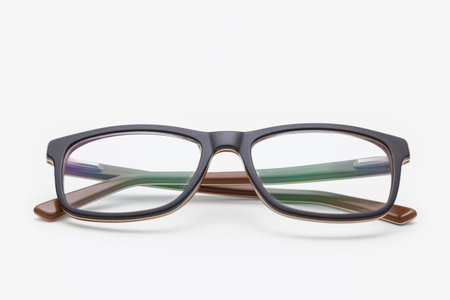 A pair of dark-rimmed glasses viewed from the front, with the temples crossed and placed on a white surface. The background is white. Sideburns are seen through the lens.の写真素材