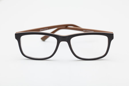 A pair of dark-rimmed glasses viewed from the front, with the temples crossed and placed on a white surface. The background is white. Part of a temple is seen through the lens.の写真素材