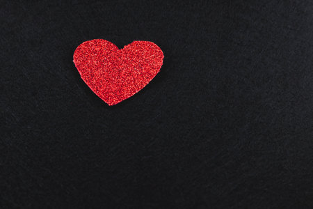 A red heart trimmed in glitter located in the upper left corner of the image on a black background. There is room for text on the right.の写真素材