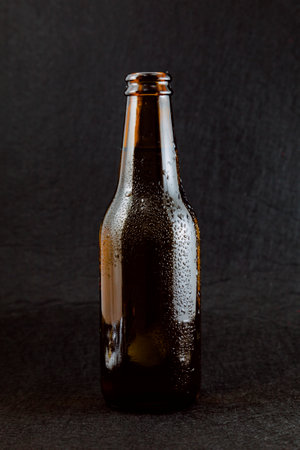 Brown bottle of fresh beer with drops of condensation on a black background. The bottle is uncovered and does not have a metal cap.の写真素材