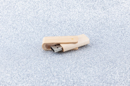 Wooden pen drive placed on a background of silver glitter, open at an obtuse angle with the USB connector pointing to the left.の写真素材