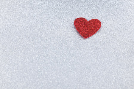 A red heart trimmed in glitter located in the upper right corner of the image on a silver glitter background. There is room for text on the left.の写真素材