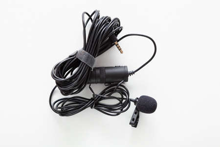 Black lapel microphone with clip and very long cable placed on a white background.