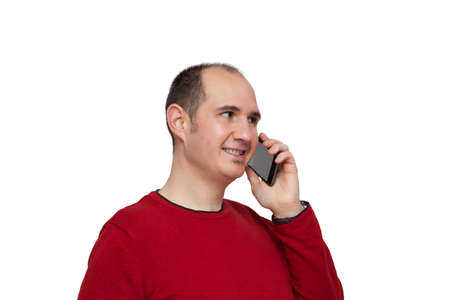 A bald young man dressed in a red sweater is holding his smartphone next to his ear with his left hand and is chatting with someone. The background is white.の写真素材