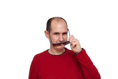 A bald young man dressed in a red sweater looking forward while with his left hand he is placing his dark glasses in front of his eyes. The background is white.の写真素材