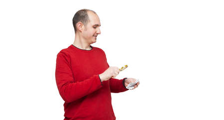A bald young man in a red sweater is reading a medicine leaflet with a magnifying glass because the print is too small. The background is white.の写真素材