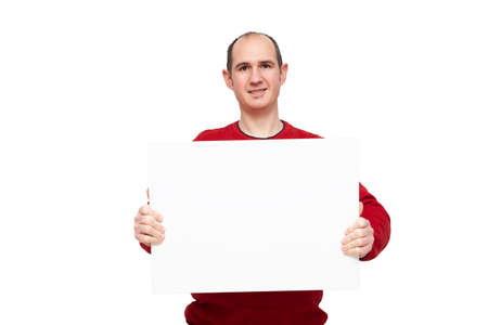 A bald young man dressed in a red sweater is holding with his hands a blank poster in front of himself placed horizontally. The background is white.の写真素材