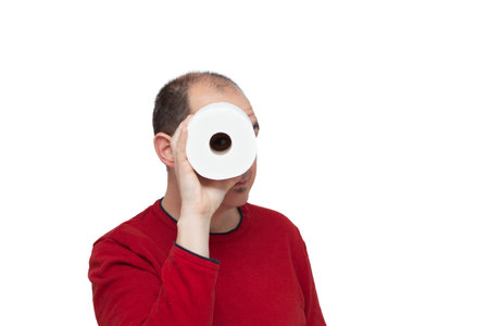 A bald young man in a red sweater peering through the toilet paper tube like a spyglass. The background is white.の写真素材