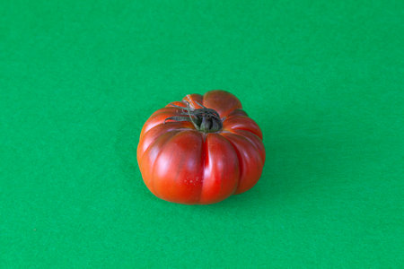 Red tomato of the raft variety isolated on a green background. The vegetable has small green leaves, wrinkles and cracks.の写真素材