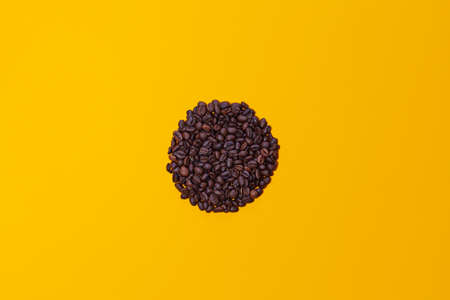 Coffee beans grouped in a circle isolated on a yellow background viewed from above. There is space for text or logos.の写真素材