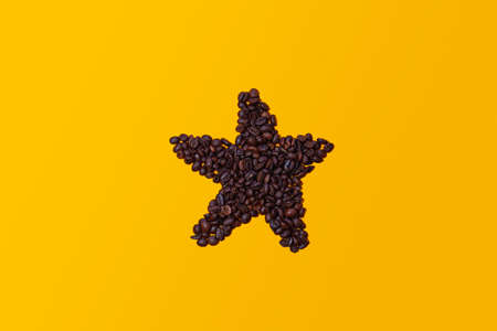Coffee beans grouped together forming the figure of a star isolated on a yellow background viewed from above. There is space for text or logos.の写真素材