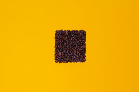 Coffee beans grouped in a rectangle isolated on a yellow background viewed from above. There is space for text or logos.の写真素材