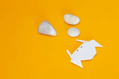 Handmade aquatic animal made using origami technique with painted eyes on a yellow surface. There is free space in the image. Next to the crab there are three round river stones.の写真素材