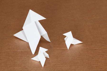 Three classic origami bird figures isolated on cardboard background, one of them is bigger and the other two are smaller.の写真素材