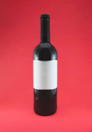 A bottle of red wine with customizable labels on a red background. The bottle is closed and has some light reflections on the glass.の写真素材