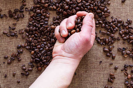 A hand of an unrecognizable man picking up coffee beans that are placed on a sackcloth.の写真素材