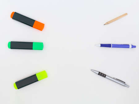 Yellow, green and orange highlighters, a pencil and two ballpoint pens on a white background.の写真素材