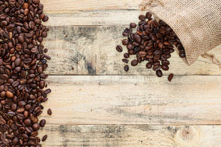 Small overturned sack from which coffee beans come out on a wooden plank surface with a margin of...