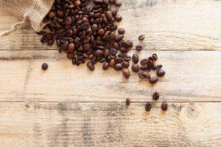 Small sack overturned on some pine wood boards where many roasted coffee beans are roasted.