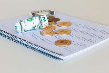 A notebook with handwritten numbers on which there are cryptocurrencies, euro and pound coins, dollar, euro and yen bills, all on a white background.の写真素材