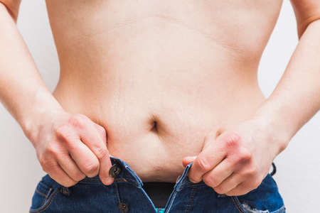 An unrecognizable fat man who can't button his jeans because his belly is too big.の写真素材