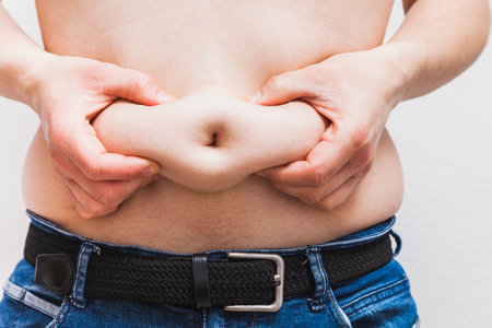 An unrecognizable fat man grabs the love handles in the navel area with both hands and squeezes.の写真素材