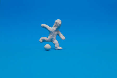 White plasticine doll practicing soccer on a blue background. The doll is ready to kick the ball hard with his right leg.の写真素材