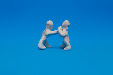 Two white plasticine dolls practicing boxing on a blue background. One doll is punching with his right fist while the other is protecting himself from the blow.の写真素材