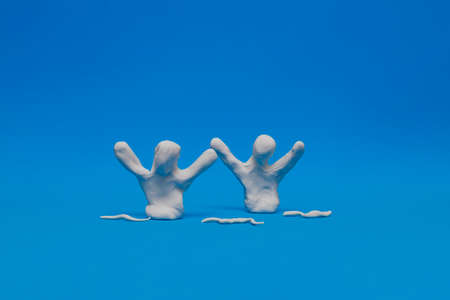 Two white plasticine dummies practicing synchronized swimming on a blue background.The dolls are performing a figure with raised arms and tilted head surrounded by plasticine waves.の写真素材