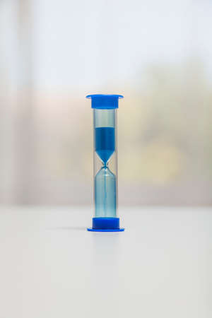 A blue hourglass on a white surface. The top part is full because the countdown has started. In the...