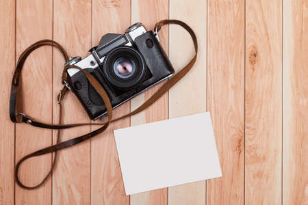 Seen from above, on some light-colored wooden boards there is an analog camera and a blank photo to customize as a mockup.の写真素材