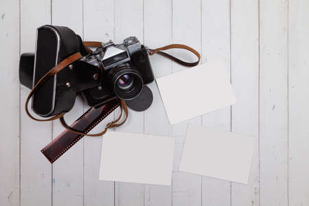 Seen from above, on white wooden boards there is an analog camera, a strip of negatives and three blank photos to customize as a mockup.の写真素材