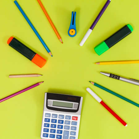 On a light green background, pointing to the center and forming an inner circle, are colored pencils, markers, highlighters, a calculator, a hole punch, a pencil and a pen.の写真素材