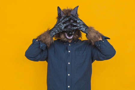 On a yellow background there is a werewolf dressed in a blue shirt is covering his eyes with his...