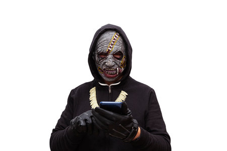 A man disguised in a zombie mask wearing a black hooded sweatshirt is touching the touch screen of a...