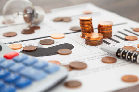 On an electricity supply bill there are three stacks of one, two and five cent coins, and other coins that are scattered around. Part of a pen, a calculator and a light bulb are also visible.の写真素材