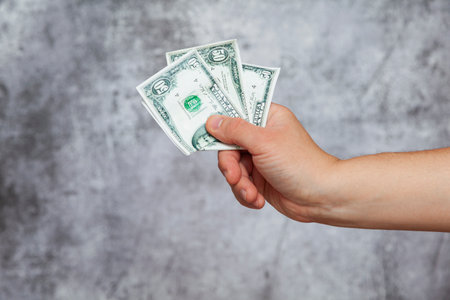 A man's right hand holding three fifty dollar bills on a textured gray background.