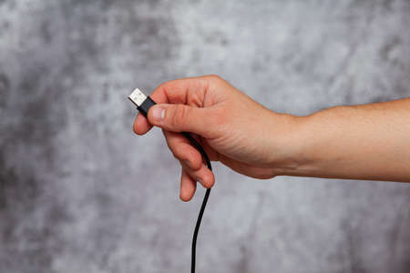 A man's right hand holding a black USB cable on a textured gray background.の写真素材