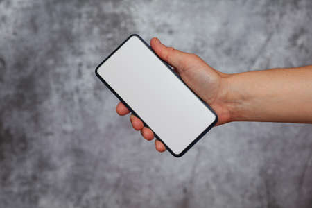 A man's right hand holding a smartphone with the screen on with white light on a textured gray background.の写真素材