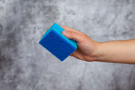 A man's right hand holding a blue scrubbing pad on a textured gray background.の写真素材