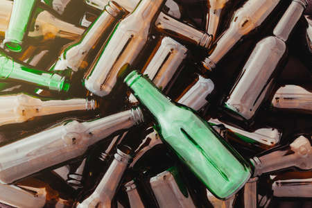 A pile of empty brown and green glass bottles. From one corner a glow of light enters.の写真素材
